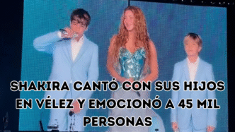 Shakira sonriendo en el escenario acompañada por sus hijos Milan y Sasha, quienes visten trajes celestes y sostienen micrófonos.